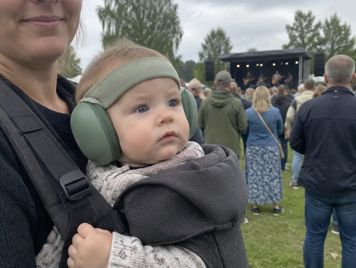 En bebis i bärsele har hörselkåpor på sig på en utomhuskonsert